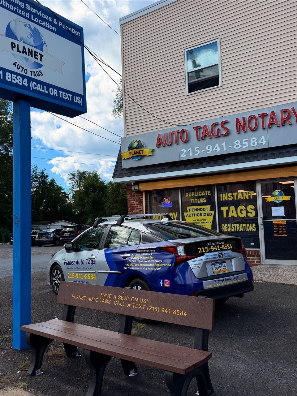 Auto Tacs Notary shop exterior with Planet Auto Tags sign and a branded vehicle on wooden platform